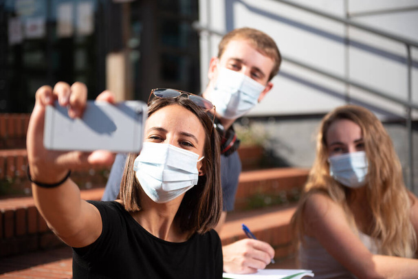 Trzech studentów w maskach do twarzy robi sobie selfie podczas pandemii coronavirus lub covid-19. - Zdjęcie, obraz