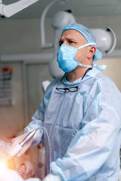 Portrait of a doctor or medical specialist. Vertical portrait. Man in scrubs. Light background with operating room. Providing operation. Closeup. - 写真・画像