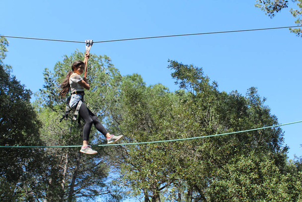 Egy fiatal lány egy kalandparkban, aki egy kötélen csúszik lefelé. - Fotó, kép