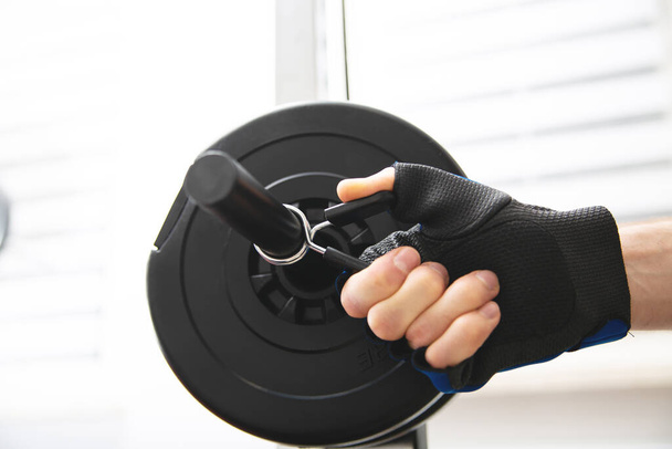 Heavy weight exercise. Close-up of a male hand in a gym glove, placing weight clamps on a dumbbell. Bodybuilding in a fitness club, home gym. Sports equipment for weight training. - Foto, afbeelding