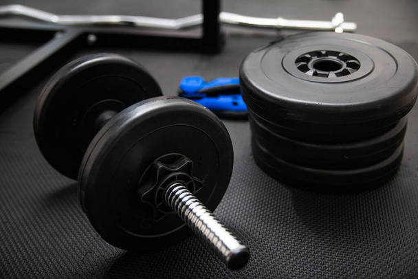 Sports equipment for weight training. Dumbbells, barbells, weights plates and weight clamps for gym bars on a dark, safe gym floor mat, on a workout room flooring. - Foto, Imagem