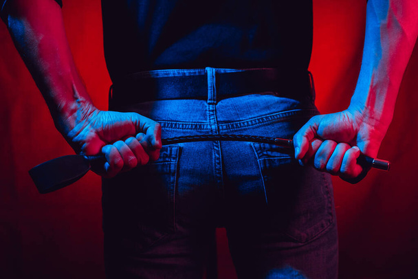 egy szexi férfi kezében egy bdsm ostor egy piros háttér a háta mögött - Fotó, kép