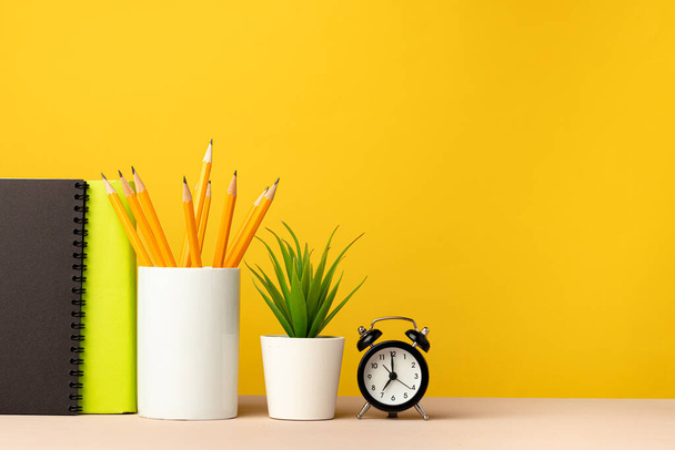 Cup of pencils and notepads on desk against yellow background - Photo, image