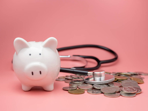 Stethoscope στο σωρό των χρημάτων και κουμπαράς σε ροζ φόντο. Σχέδιο δημοσιονομικού ελέγχου υγείας, κρίση χρέους και χρηματοοικονομικής κρίσης. - Φωτογραφία, εικόνα