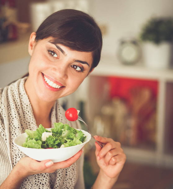 Young woman eating fresh salad in modern kitchen - Fotó, kép