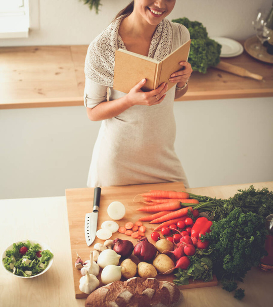 Young woman reading cookbook in the kitchen, looking for recipe - Foto, afbeelding