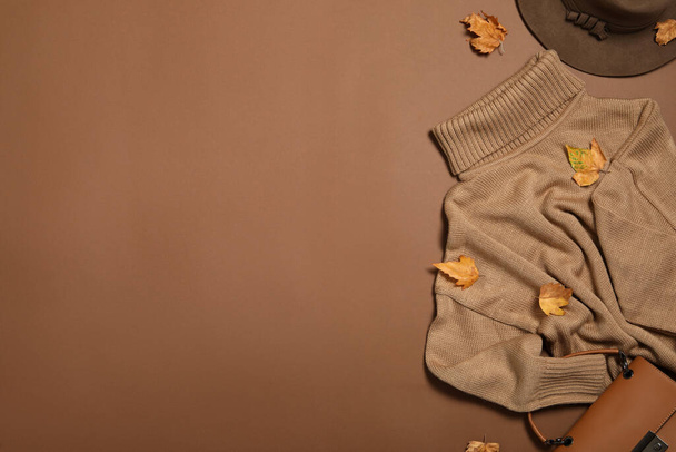 Flat lay composition with sweater and dry leaves on brown background, space for text. Autumn season - Fotó, kép