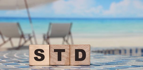 木製のブロックは、リラックスした海のビーチの風景の背景に単語STDを形成します。医療の概念.. - 写真・画像