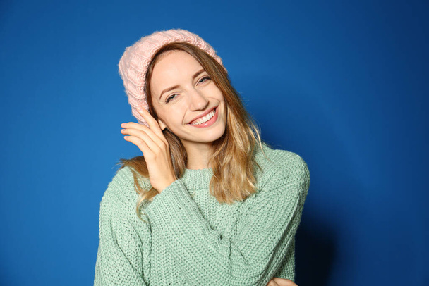 Mujer joven feliz con suéter cálido y sombrero de punto sobre fondo azul - Foto, Imagen