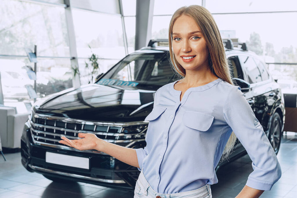 Attractive young female car dealer standing in showroom - Photo, Image