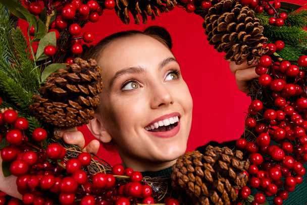 Close-up portrait of her she nice attractive pretty cute glad impressed dreamy cheerful cheery girl looking through festal green wreath isolated bright vivid shine vibrant red color background - Φωτογραφία, εικόνα