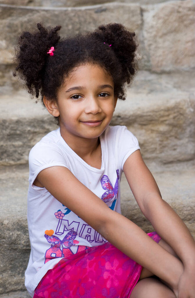 Маленька коричнева дівчина афроамериканка з кучерявим волоссям сміється голосно і дивиться на камеру - Фото, зображення