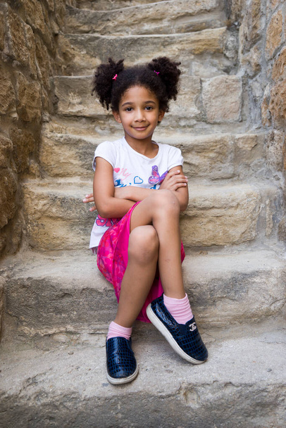 Маленькая коричневая девочка афроамериканская внешность с кудрявыми волосами смеется вслух и смотрит в камеру - Фото, изображение