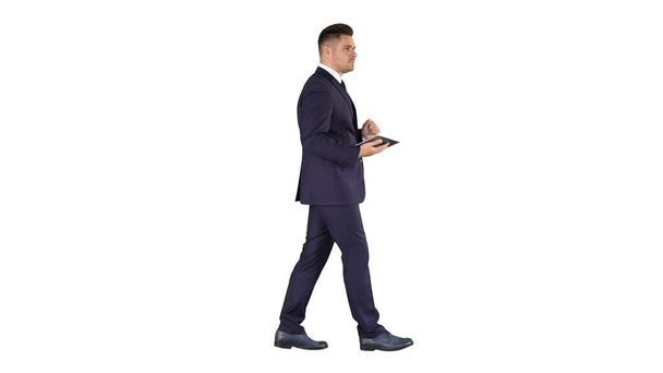 Elegant young businessman using his PC tablet while walking on white background. - Foto, afbeelding