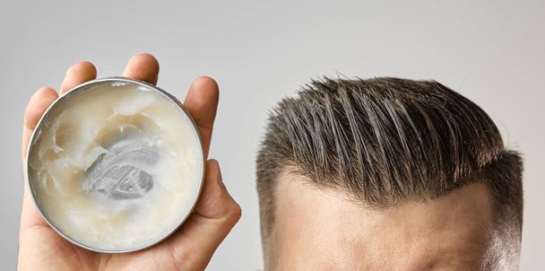Man applying a clay, pomade, wax, gel or mousse from round metal box for styling his hair after barbershop hair cut. Advertising concept of mans products. Treatment and care against lost of hair - Photo, Image