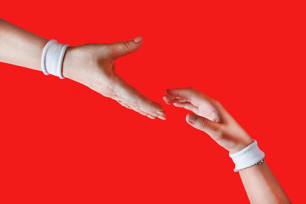 Hilfe leisten. Helfende Hand für einen Freund. Hände mit weißen Armbändern auf rotem Hintergrund. - Foto, Bild