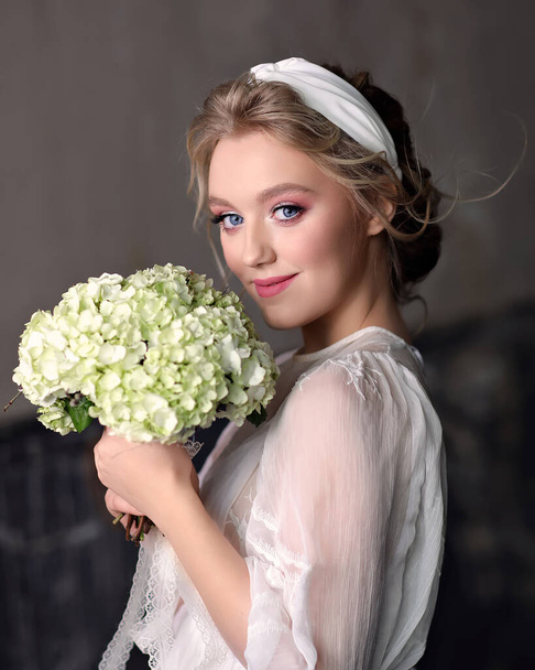 Slender bride in vintage wedding dress in the Studio. Portrait of a smiling girl with a wedding bouquet in her hands - Фото, изображение