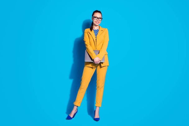 Full length photo of attractive business lady worker hold laptop online meeting wear spectacles yellow blazer suit dotted blouse shirt high-heels isolated bright blue color background - Foto, Imagen