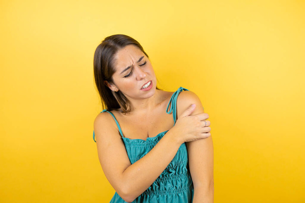 Junge schöne Frau auf isoliertem gelben Hintergrund mit Schmerzen an der Schulter und einem schmerzhaften Gesichtsausdruck - Foto, Bild