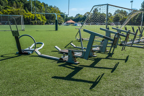 Un trineo de entrenamiento de fútbol sentado en césped artificial no utilizado en un campo de fútbol y fútbol en un parque deportivo en un día soleado brillante a finales de verano - Foto, Imagen