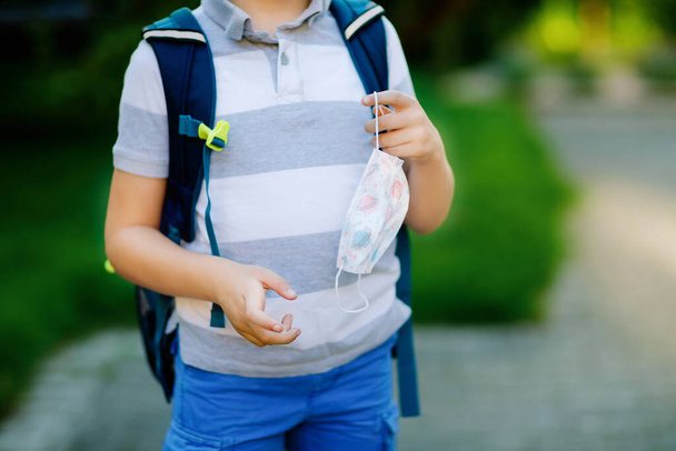 Close-up of kid boy with medical mask and backpack or satchel. Schoolkid on way to school. child outdoors. Back to school after quarantine time from corona pandemic disease lockdown. no face. - 写真・画像