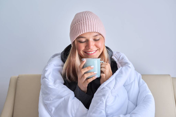 Κρύο χειμώνα φθινόπωρο, έφηβος κορίτσι κάθεται στον καναπέ κάτω από ζεστή κουβέρτα - Φωτογραφία, εικόνα