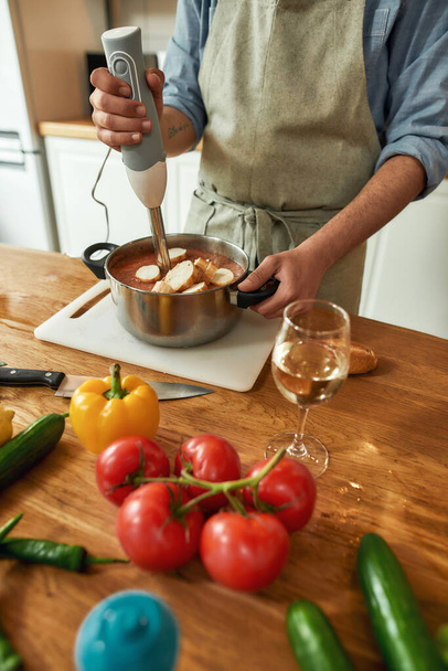 キッチンでイタリア料理を準備しながら、人の作物のショット、シェフは、手ブレンダーを使用して調理し、刻んだ野菜やパンをブレンド - 写真・画像