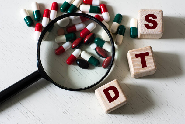 STD (Sexually Transmitted Diseases) - a word on cubes on a light background with a magnifying glass and tablets. Medical concept - Photo, Image