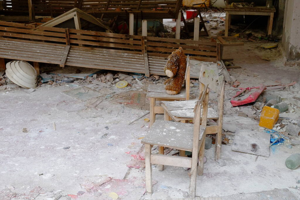 Sucio juguete de peluche en la silla. Un oso de peluche sin cabeza en un jardín de infantes abandonado en Pripyat. - Foto, Imagen