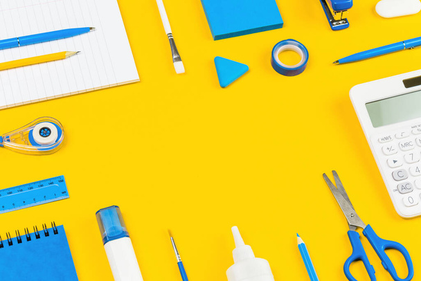 Assorted office supplies and school white and blue stationery on bright yellow background border. Organized knolling for back to school or education and craft concept. Selective focus. Copy space - Photo, Image