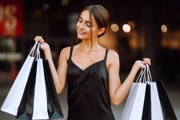 Fashion woman enjoying shopping. Elegant woman wears black dress holding black and white shopping bags. Black friday, sale, consumerism, lifestyle concept. - Photo, Image