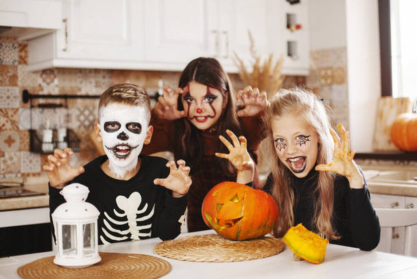 幸せな子供たちは、衣装を着た家で台所でハロウィンを祝い、カボチャのランタンで構成されていますジャックはカメラを見て笑顔. - 写真・画像