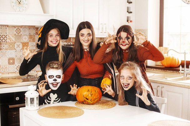 Щасливі діти святкують Хелловін на кухні в костюмах і гримі з гарбузовим ліхтарем Джеком, який дивиться на камеру і посміхається - Фото, зображення