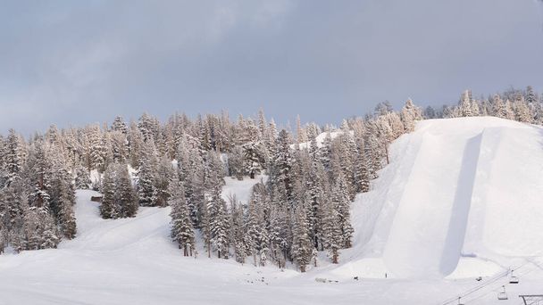 Pusta halfpipe w ośrodku narciarskim na szczycie zaśnieżonej góry w pochmurny, zimowy poranek. - Zdjęcie, obraz