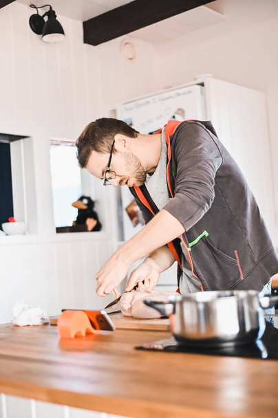 attractive nerd guy with glasses in stylish kitchen follows a recipe on the phone prepares chicken - Φωτογραφία, εικόνα