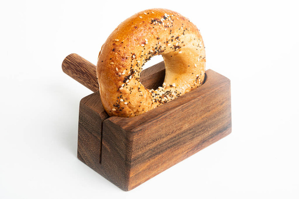 A single freshly baked bagel propped on a wood slicing stand set on a plain white background. - Photo, Image