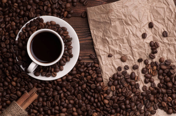 Kaffeetasse mit Kaffeebohnen auf Textil und Zimt auf dunklem Holz Hintergrund Tisch mit Papier - Foto, Bild