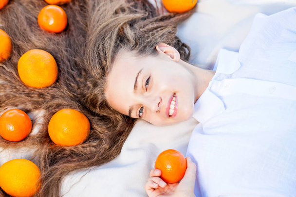 Young teenage girl lies on a blanket on the lawn with oranges in her hair - Fotoğraf, Görsel
