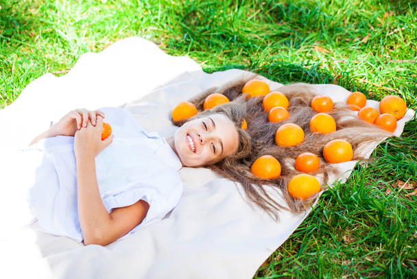 Young teenage girl lies on a blanket on the lawn with oranges in her hair - Photo, Image