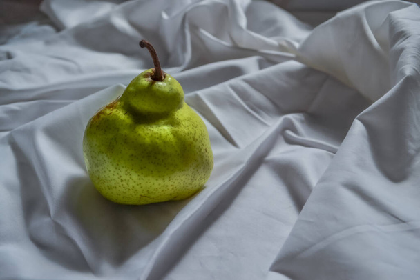 ripe green pear on white cloth with folds in light of sun - Φωτογραφία, εικόνα
