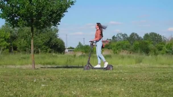Jonge mooie vrouw rijdt op een elektrische scooter door het park en de groene omgeving, op sommige foto 's heeft ze de wind in haar haar. - Video