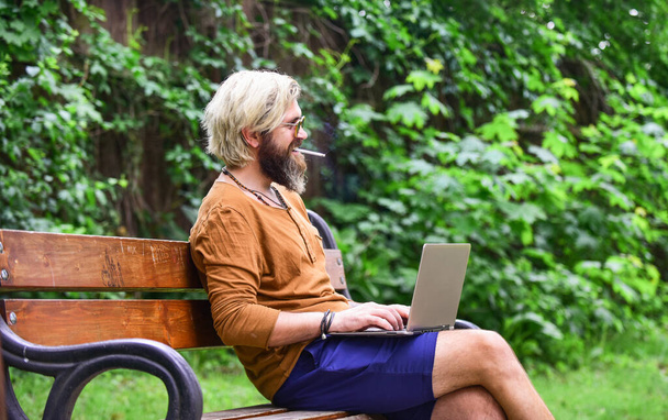 ノートパソコンを持ったビジネスマンが公園のベンチに座ってる。ノートパソコンで働いてるハンサムな男。ビジネスマンはコンピューターを使って屋外で働いています。ビデオ会議を始めろ。ビデオ通話での通信。知識に向かって - 写真・画像