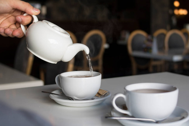 The guy pours tea into a white cup from a white teapot - Фото, зображення