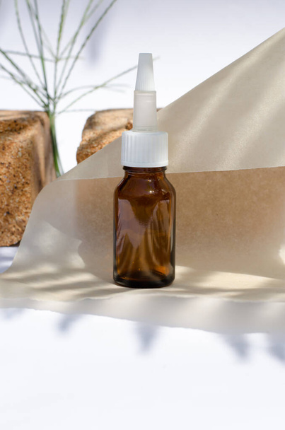 Brown bottle on a background of stones and parchment paper with shadows. Cosmetic oils. - Photo, Image
