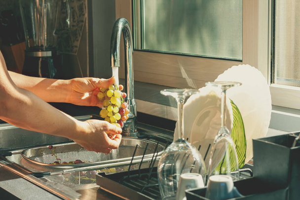 Női kézmosás fürtök betakarított érett és lédús zöld szőlő a konyhában. Egészséges táplálkozás életmód koncepció - Fotó, kép