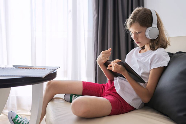 Girl studies online at home, child with digital tablet in headphones - Photo, image