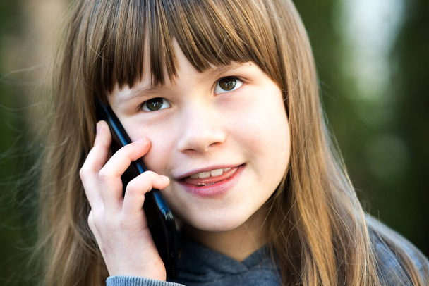 Portret ładnej dziewczynki z długimi włosami rozmawiającej przez komórkę. Mała dziewczynka komunikująca się za pomocą smartfona. Koncepcja komunikacji dzieci. - Zdjęcie, obraz