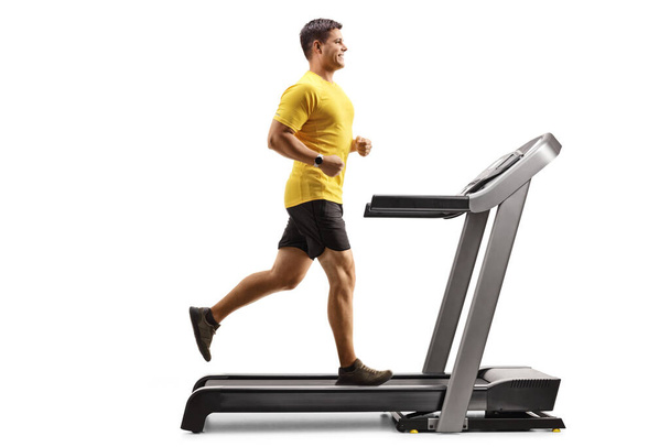 Full length profile shot of a strong young man running on a treadmill isolated on white background - Fotoğraf, Görsel