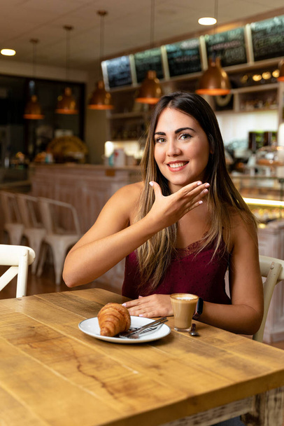 Молодая женщина пьет кофе, делая знак слушателя. - Фото, изображение