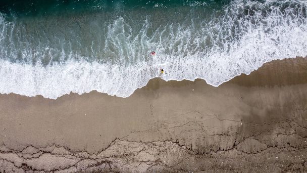 Due bambini che giocano sulle onde alla spiaggia di Agios Ioannis, nella penisola di Pelion, Grecia. Foto scattata con drone. - Foto, immagini